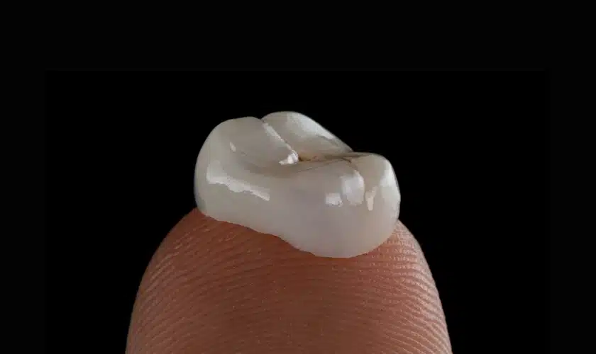 A finger tip holding a dental crown, representing affordable dental care and prioritizing oral health.